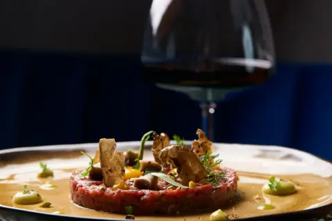 Tartare di manzo raffinata, guarnita con crostini e verdure, pronta per un perfetto abbinamento vino.