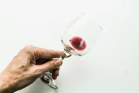 Mano che tiene un bicchiere di vino rosso con residui sul fondo, dove si nota l'acido tartarico.