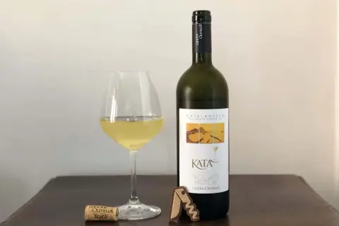 Un bicchiere di vino bianco e una bottiglia di Catalanesca del Vesuvio, con tappo e cavatappi sul tavolo.