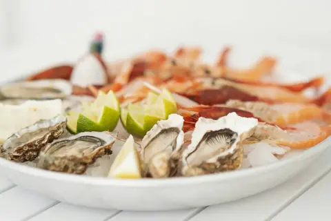 Piatto di ostriche fresche e gamberi, guarnito con spicchi di limone e lime. Un delizioso pesce bianco pronto da gustare.