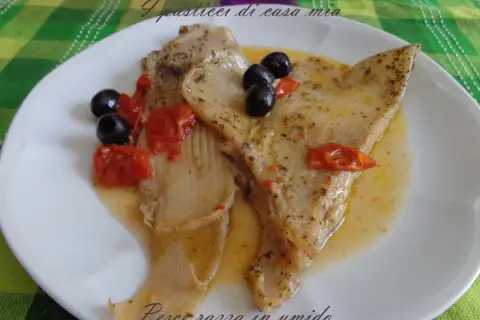 Piatto di pesce razza in umido con pomodorini e olive nere, condito con erbe aromatiche.
