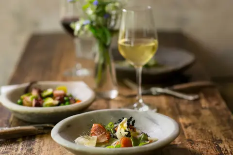Un bicchiere di vino bianco per cucinare accompagna un pasto raffinato con piatti di pesce e verdure su un tavolo di legno rustico.