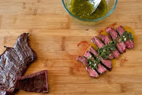 Fetta di manzo che carne è, succulenta e affettata, condita con salsa verde su tagliere di legno.