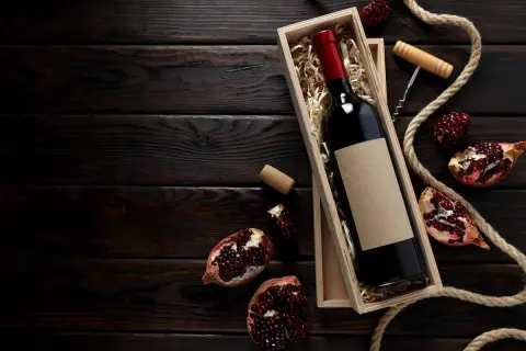 Una bottiglia di vino rosso in una scatola di legno, circondata da melograni e corda. Un assaggio dei **vini campani** più pregiati.