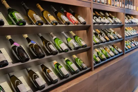 Scaffali pieni di bottiglie di champagne, alcune con etichette dorate e verdi. Una bottiglia da 5 litri nome è visibile in primo piano.