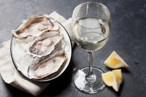 Un piatto di ostriche fresche su ghiaccio, accompagnato da un bicchiere di vino bianco frizzante e spicchi di limone. Un'elegante degustazione di ostriche e vino.