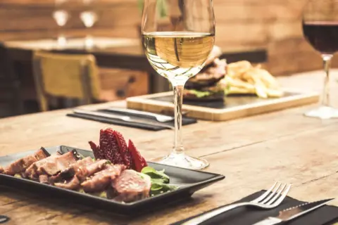 Un bicchiere di vino bianco, perfetto vino bianco per carne alla brace, accanto a un piatto di carne affettata e fragole su un tavolo di legno.