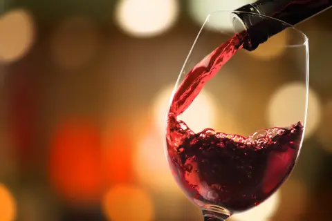 Versare vino rosso in un bicchiere, un momento allappante significato di piacere e convivialità, con luci sfocate sullo sfondo.