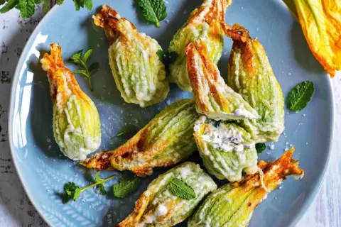 Fiori di zucca fritti, ripieni di formaggio cremoso e guarniti con menta fresca, su un piatto blu.