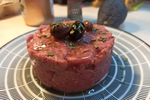 Un delizioso tartare di carne cruda, guarnito con olive nere e erba cipollina, pronto per essere gustato.