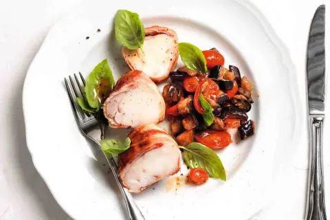 Tranci di rana pescatrice avvolti nel prosciutto, serviti con ratatouille di verdure e basilico fresco.