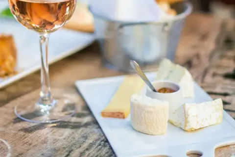 Calice di vino rosato accanto a un tagliere di formaggi, con un assaggio di passito di Pantelleria.