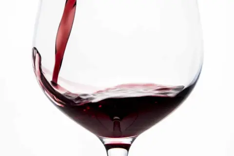 Vino rosso porpora versato in un calice, creando un vortice invitante.