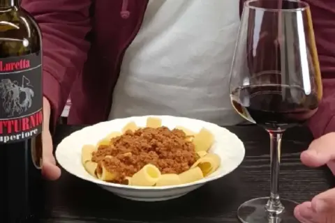 Un bicchiere di vino rosso e un piatto di pasta al ragù, accompagnati da una bottiglia di Gutturnio.