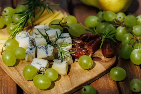 Un tagliere di legno con formaggio erborinato, uva verde succosa, datteri e rosmarino. Un perfetto abbinamento uva e formaggio per un aperitivo.