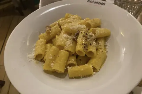 Piatto di rigatoni alla carbonara, conditi con guanciale croccante, pecorino romano e pepe nero. Perfetto con un bicchiere di vino bianco secco.
