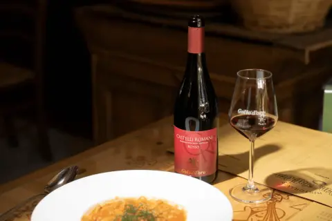 Bottiglia di vino rosso e bicchiere su un tavolo di legno, con un piatto di pasta. Consigli per come conservare il vino rosso.