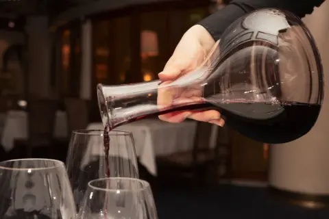 Mano versa vino rosso da una caraffa in bicchieri trasparenti, creando un'atmosfera elegante.