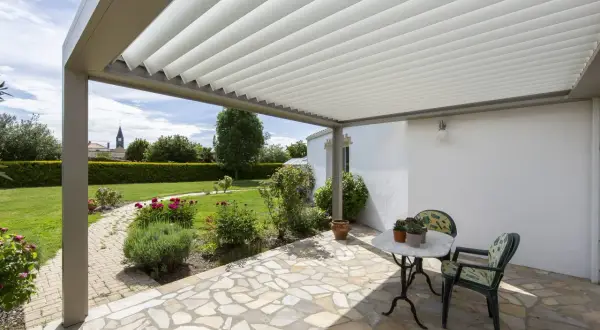 Un angolo relax sotto una vite a pergola semplice, con un tavolino e sedie, affacciato su un giardino fiorito.