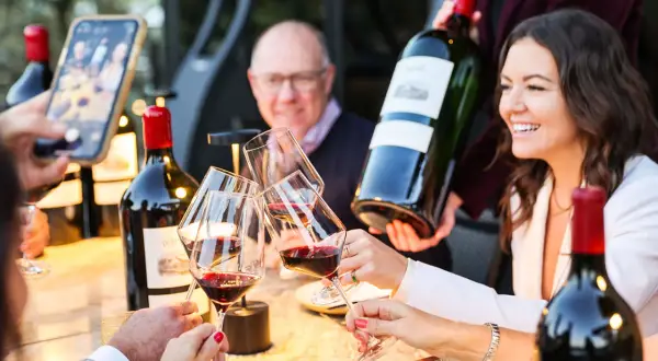 Brindisi con vino rosso, una bottiglia da 12 litri nome in mano, mentre si scatta una foto con lo smartphone.