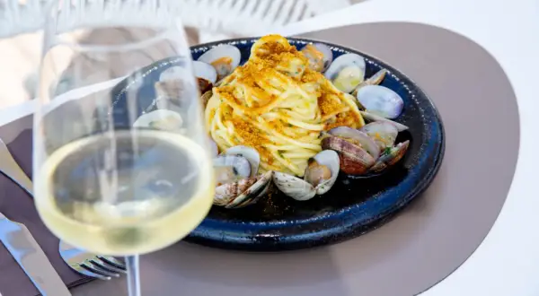 Un bicchiere di vino bianco, perfetto vino bianco da abbinare al pesce, accanto a un piatto di spaghetti alle vongole.