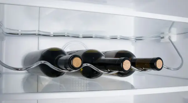 Bottiglie di vino bianco su un ripiano cromato all'interno di un frigorifero.