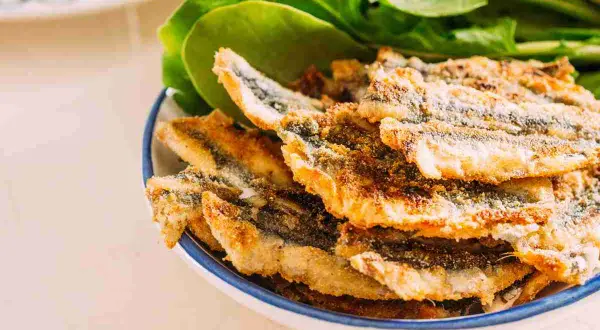 Piatto di alici fritte dorate e croccanti, servite con foglie verdi fresche.