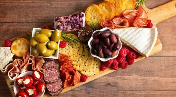 Un invitante tagliere di formaggi misti, salumi, olive, lamponi e crostini, perfetto per un aperitivo.