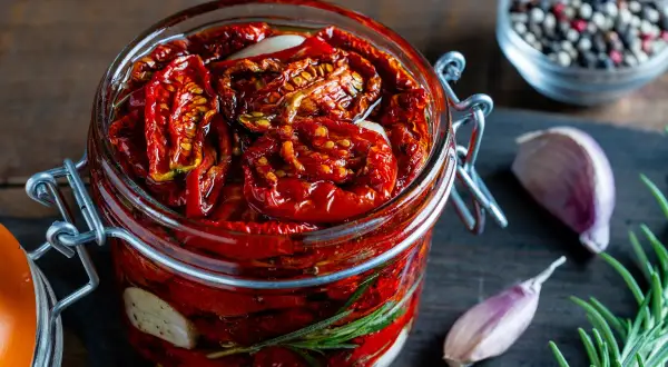 Pomodori secchi sott'olio in un barattolo, con aglio e rosmarino. Un sapore intenso che evoca l'umami, significato di gusto profondo.