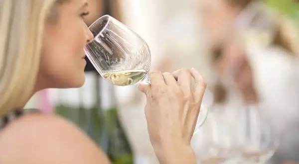 Donna bionda assapora un vino bianco, forse un vino 15 gradi, in un ambiente conviviale.