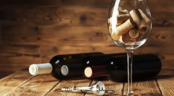 Calici pieni di tappi, bottiglie e cavatappi su un tavolo di legno. Un promemoria visivo dell'ossidazione del vino e del tempo che passa.