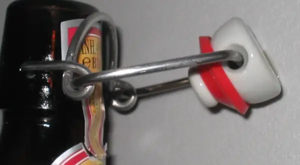 La bottiglia che si stappa da sola, con il suo tappo a scatto in ceramica bianca e rossa, evoca un senso di attesa e liberazione.