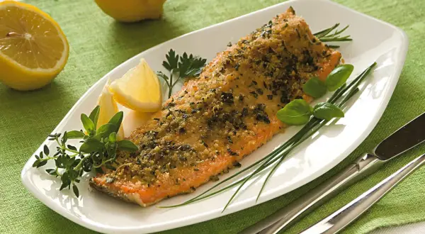 Filetto di trota salmonata cotto al forno con erbe aromatiche e limone, servito su un piatto bianco con guarnizioni fresche.