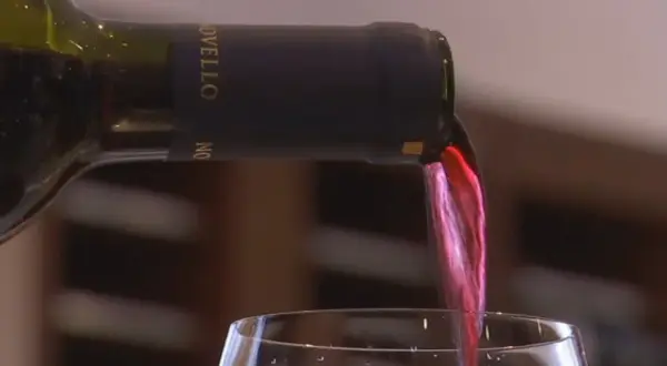 Versando vino rosso da una bottiglia con tappo a vite. Il liquido scorre nel bicchiere, creando un'onda cremisi.