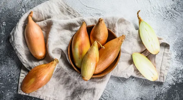 Scalogno cos'è? Cipolle allungate, dorate e verdi, alcune intere, altre tagliate a metà, su un panno di lino.