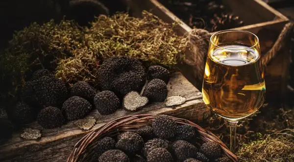 Truffles in a basket and on a wooden board, with a glass of white wine. La domanda è: che vino abbinare al tartufo?