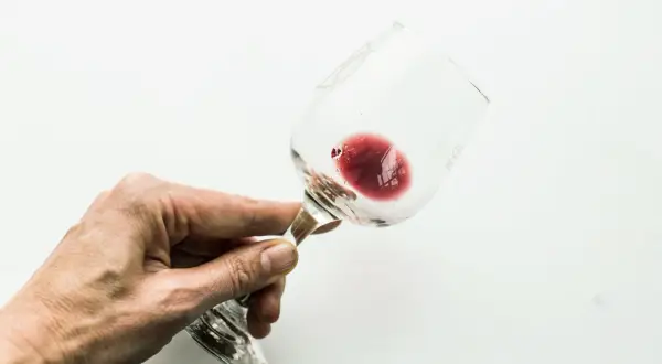 Mano che tiene un bicchiere di vino rosso con residui sul fondo, dove si nota l'acido tartarico.