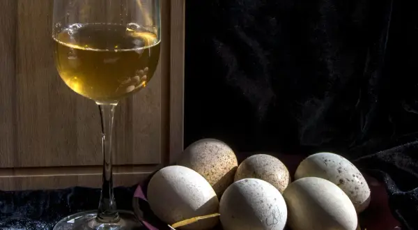 Un calice di vino dorato e un piatto di uova rustiche, un'idea su cosa abbinare alle uova per un pasto semplice e gustoso.