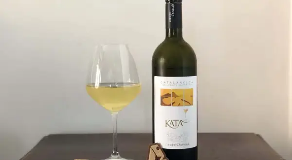 Un bicchiere di vino bianco e una bottiglia di Catalanesca del Vesuvio, con tappo e cavatappi sul tavolo.