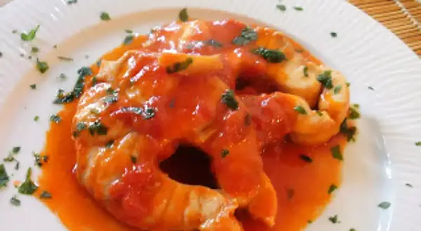 Due fette di pesce palombo cotte in salsa di pomodoro e guarnite con prezzemolo tritato, servite su un piatto bianco.
