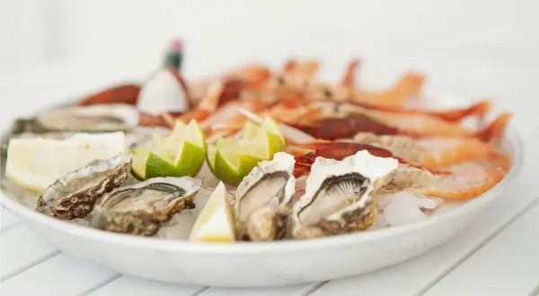 Piatto di ostriche fresche e gamberi, guarnito con spicchi di limone e lime. Un delizioso pesce bianco pronto da gustare.