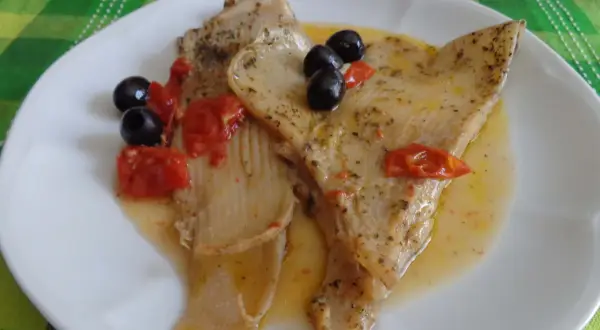Piatto di pesce razza in umido con pomodorini e olive nere, condito con erbe aromatiche.