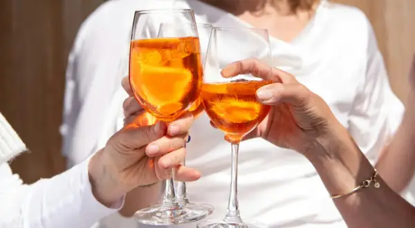 Tre mani brindano con bicchieri di Spritz arancione, un momento di gioia e leggerezza, pensando alle calorie spritz.