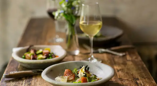 Un bicchiere di vino bianco per cucinare accompagna un pasto raffinato con piatti di pesce e verdure su un tavolo di legno rustico.