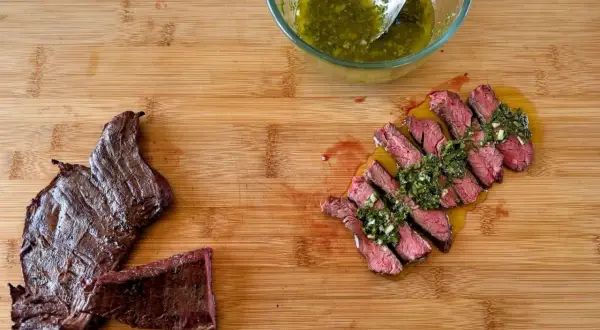 Fetta di manzo che carne è, succulenta e affettata, condita con salsa verde su tagliere di legno.