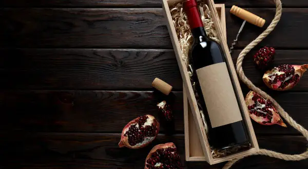 Una bottiglia di vino rosso in una scatola di legno, circondata da melograni e corda. Un assaggio dei **vini campani** più pregiati.