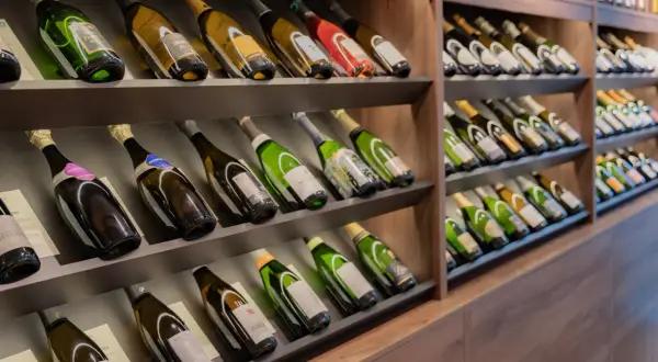 Scaffali pieni di bottiglie di champagne, alcune con etichette dorate e verdi. Una bottiglia da 5 litri nome è visibile in primo piano.