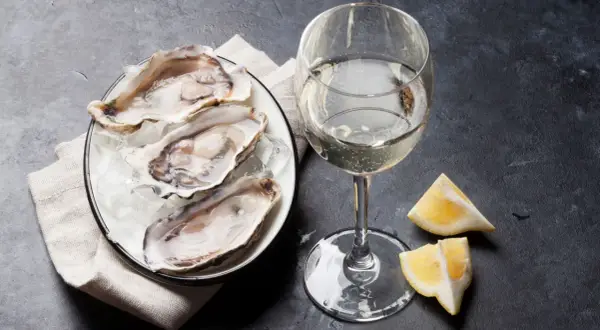 Un piatto di ostriche fresche su ghiaccio, accompagnato da un bicchiere di vino bianco frizzante e spicchi di limone. Un'elegante degustazione di ostriche e vino.