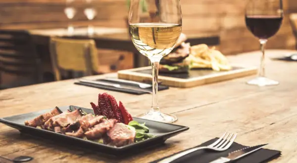 Un bicchiere di vino bianco, perfetto vino bianco per carne alla brace, accanto a un piatto di carne affettata e fragole su un tavolo di legno.