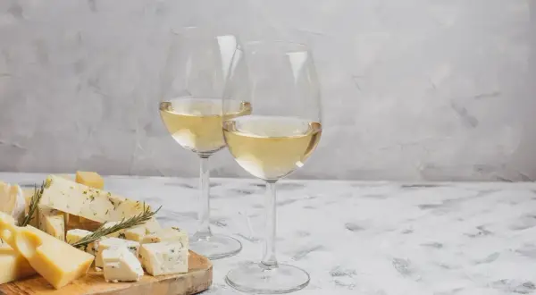 Due calici di vino bianco, perfetti per accompagnare un tagliere di formaggi misti, tra cui erborinato e stagionato.